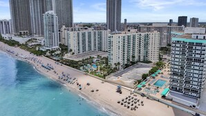 A coastal cityscape with high-rise buildings, a sandy beach, and a swimming pool area. - Beachfront Getaway | Direct Ocean Views + Balcony (Hollywood)