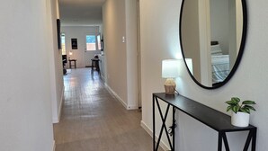 A hallway with a wooden floor, a black console table with a lamp and a plant, and a large mirror on the wall. - Cute Brand New Home in McKinney (McKinney)