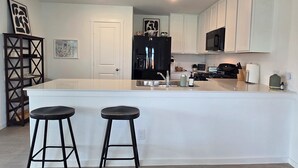 A modern kitchen with white cabinetry, a central island with stools, a black refrigerator, and a microwave above the stove. - Cute Brand New Home in McKinney (McKinney)