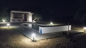 A modern building with a swimming pool, surrounded by well-lit areas and a few trees. - House and pool (Fontenilles)
