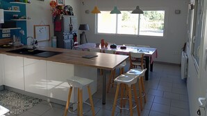 A modern kitchen with a central island, bar stools, a dining table, and a large window providing natural light. - House and pool (Fontenilles)