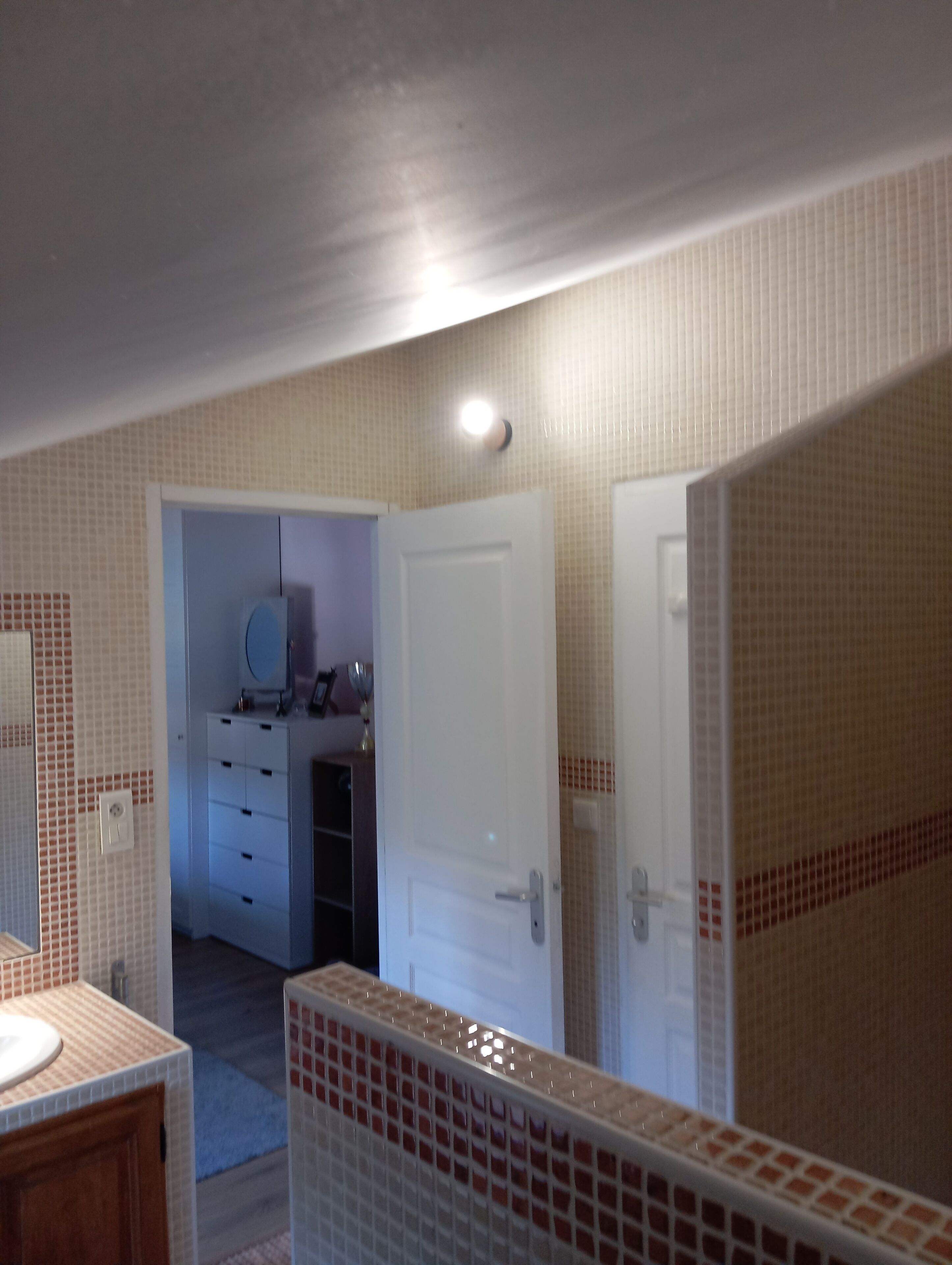 Casa de banho com chão em mosaico, lavatório e espelho. Há uma porta que dá para outro quarto.