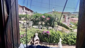 A view through a window with a mesh screen, displaying a garden with various plants and a statue. - Residenza Rio Elba: peace in Elba’s nature (Rio dell'Elba)