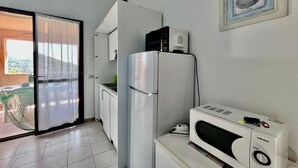 A compact kitchen with a refrigerator, microwave, and a small window with a picture frame. - Residenza Rio Elba: peace in Elba’s nature (Rio dell'Elba)