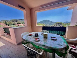 A balcony with a table set for two, overlooking a scenic landscape with hills and a clear sky.