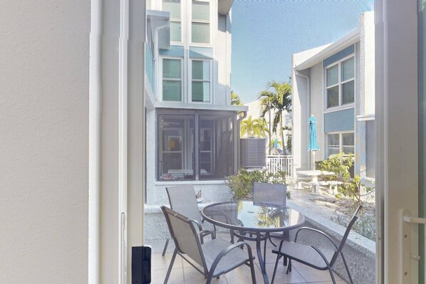 A glass door leading to a patio with a round table and chairs, surrounded by plants and a blue umbrella.