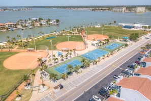 Vista aérea de um complexo esportivo com um campo de beisebol, quadras de tênis e um estacionamento.