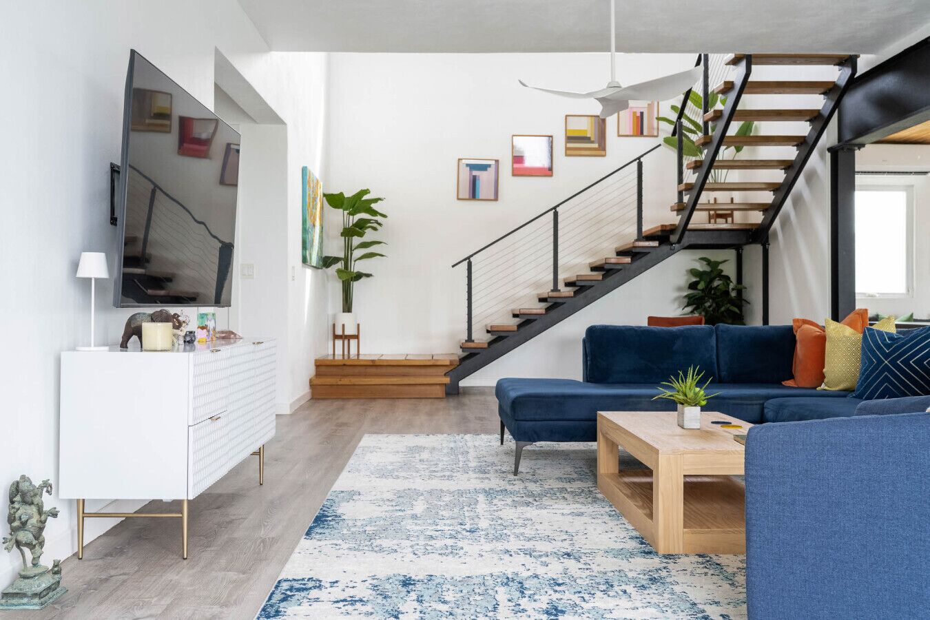 A modern living room with a staircase, a sofa, a coffee table, and a TV.