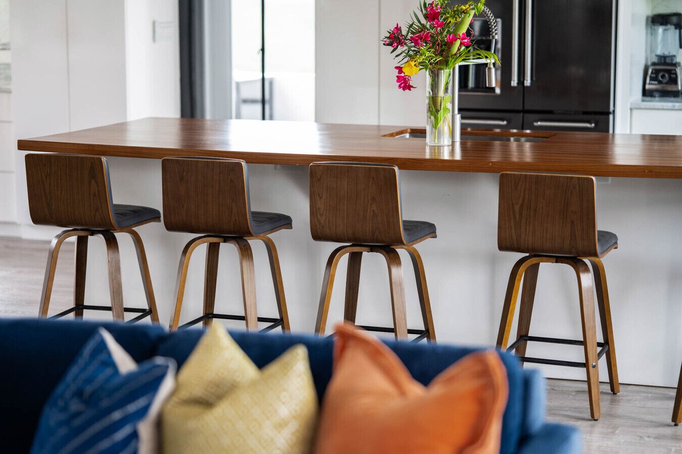 A modern kitchen with a wooden island, four bar stools, and a vase of flowers.