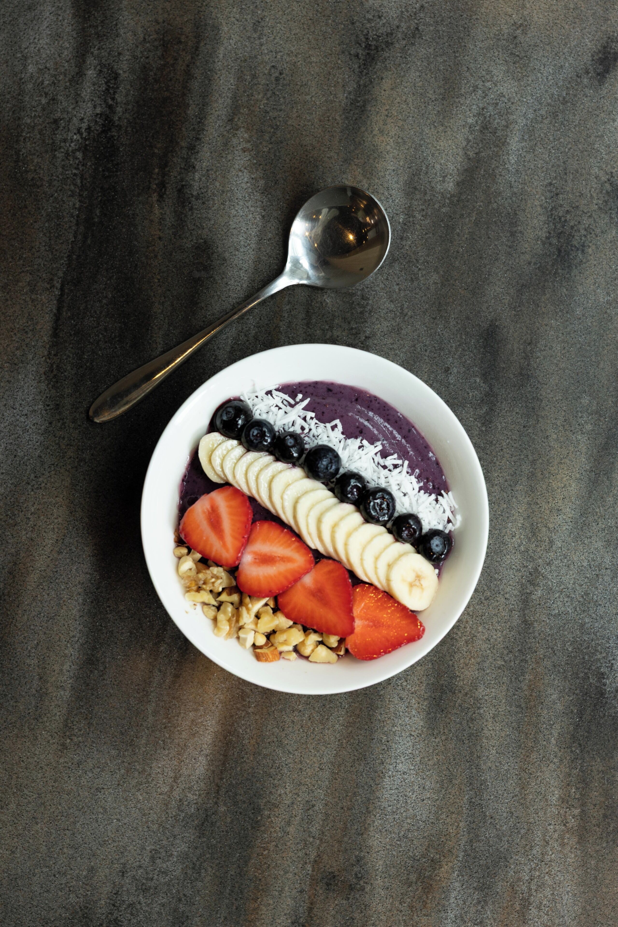 A bowl of fruit and granola on a textured surface.