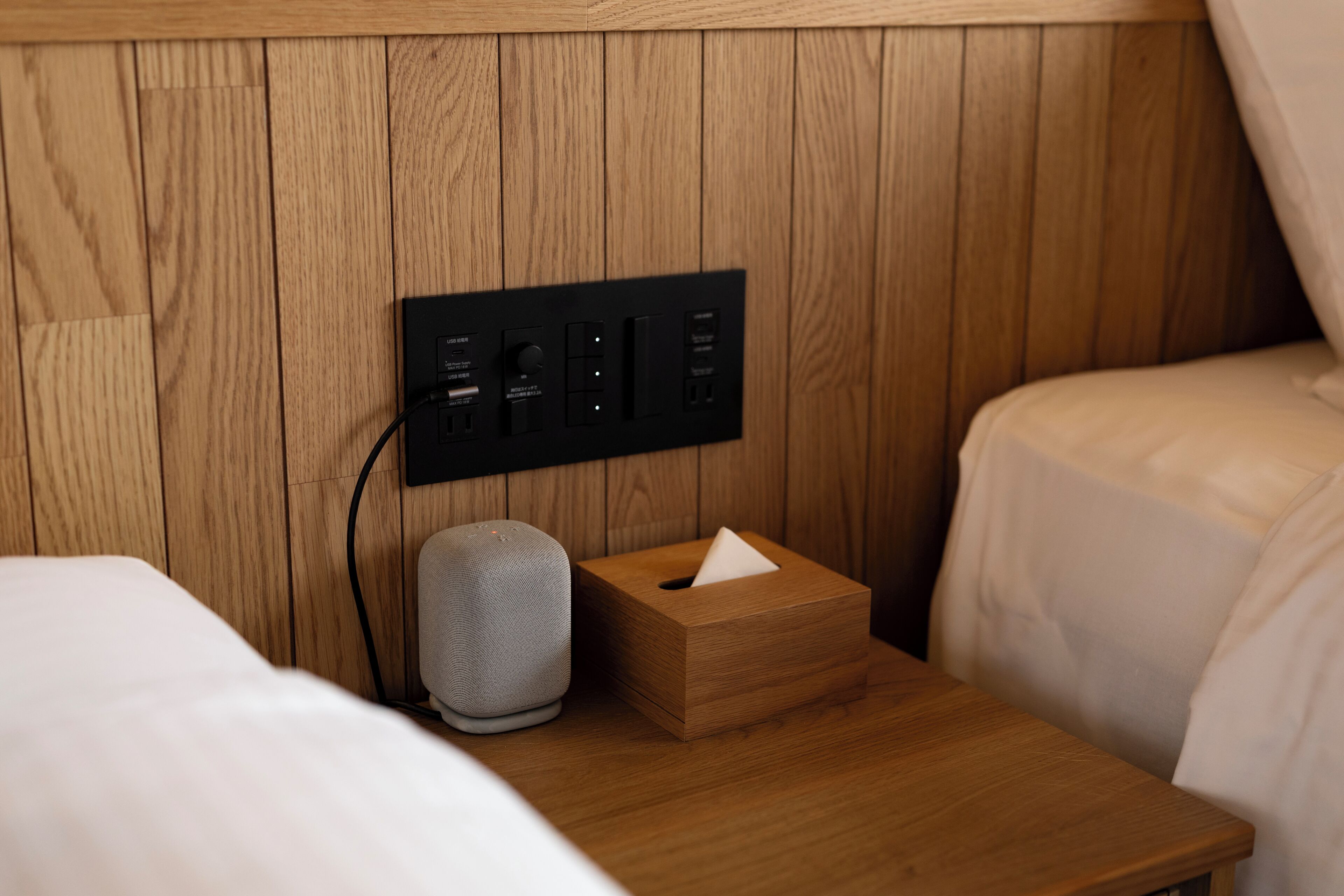 A wooden panel wall with a power strip, a speaker, and a tissue box on a bedside table.