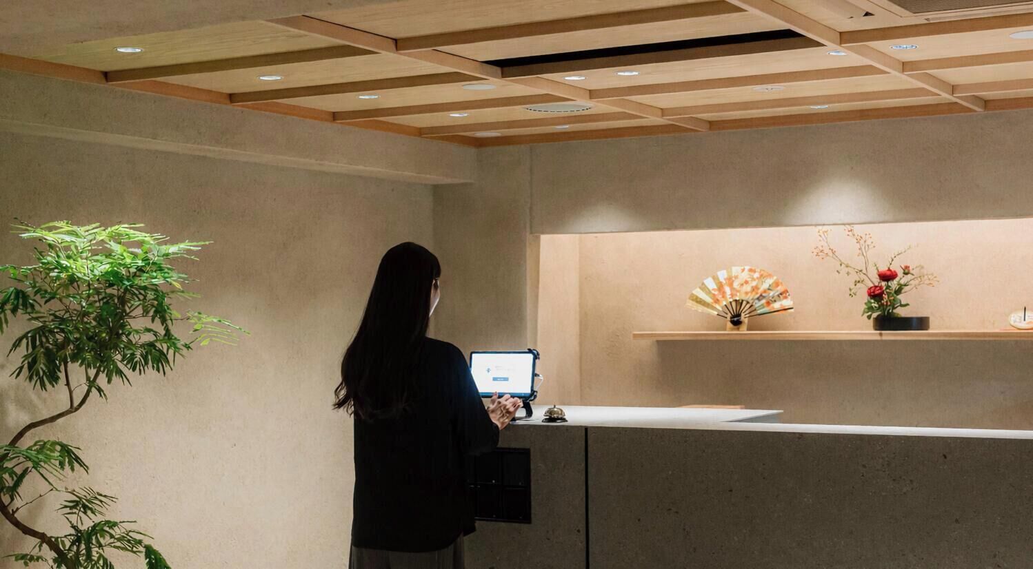 A reception desk with a computer, a plant, and a decorative fan on a shelf.