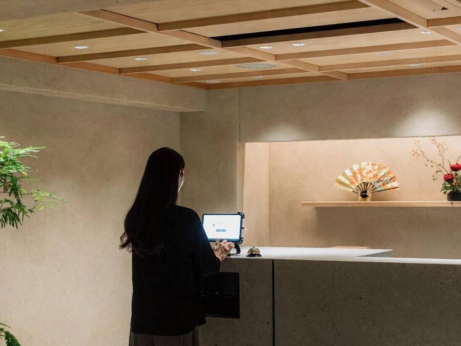 A reception desk with a computer, a plant, and a decorative fan on a shelf.