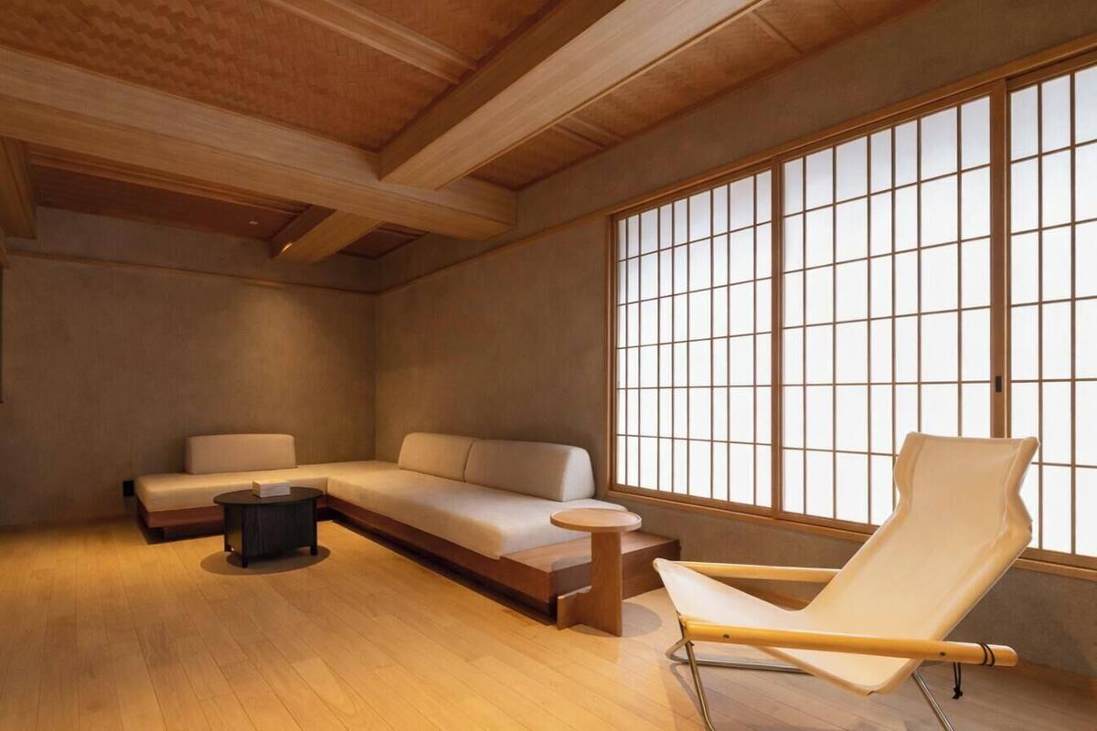 A modern interior with a wooden ceiling, a sofa, a chair, and a large window with grid panes.