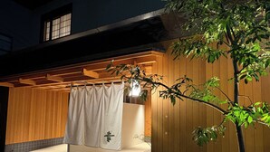 A Japanese-style outdoor bath area with a wooden deck, a white towel hanging, and a potted plant.