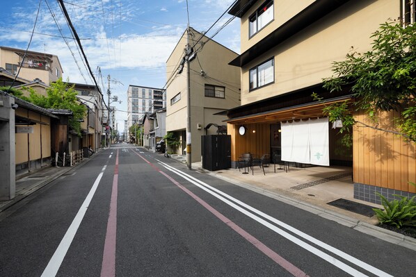 Une rue bordée d’immeubles, un restaurant avec une terrasse, et un ciel dégagé.