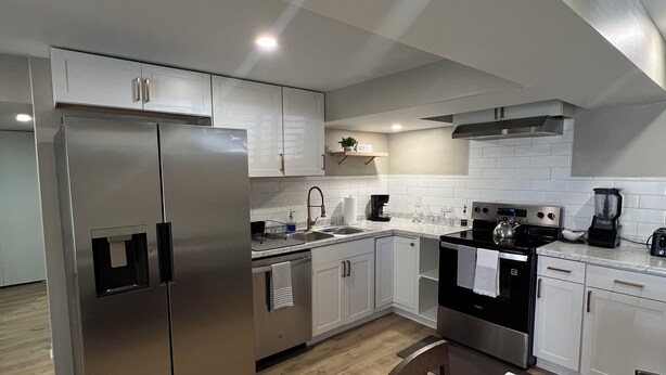 A modern kitchen with stainless steel appliances, white cabinetry, and a wooden dining table. - Charming 2-bed, 2 full bath lower level studio with WiFi, AC in Ardmore (Winston-Salem)