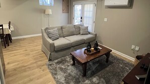 A living room with a grey sofa, a wooden coffee table, and a grey rug. - Charming 2-bed, 2 full bath lower level studio with WiFi, AC in Ardmore (Winston-Salem)