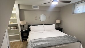 A bedroom with a bed, bedside lamps, a ceiling fan, a window, and a built-in shelf with towels. - Charming 2-bed, 2 full bath lower level studio with WiFi, AC in Ardmore (Winston-Salem)