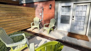 A house with a covered patio area, outdoor seating with chairs, a brick wall, and a white door with a window. - Charming 2-bed, 2 full bath lower level studio with WiFi, AC in Ardmore (Winston-Salem)