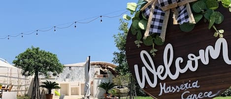 Un letrero de madera con la inscripción 'Welcome' y 'Hassia Cayce', rodeado de follaje y luces de adorno.