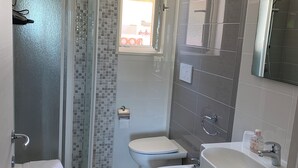 Ein modernes Badezimmer mit Duschkabine aus Glas, Toilette, Bidet und Waschbecken mit Spiegel.