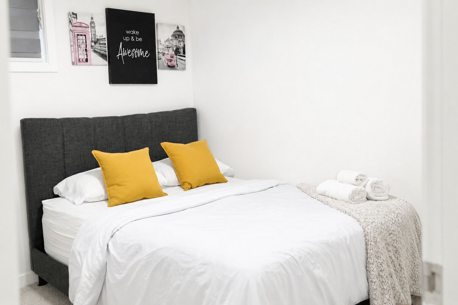 A neatly made bed with white and mustard pillows, a grey headboard, and a white blanket.