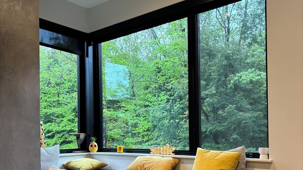 Un intérieur moderne avec une grande fenêtre, un banc en bois agrémenté de coussins et une table décorée de bougies et d’un verre à vin.