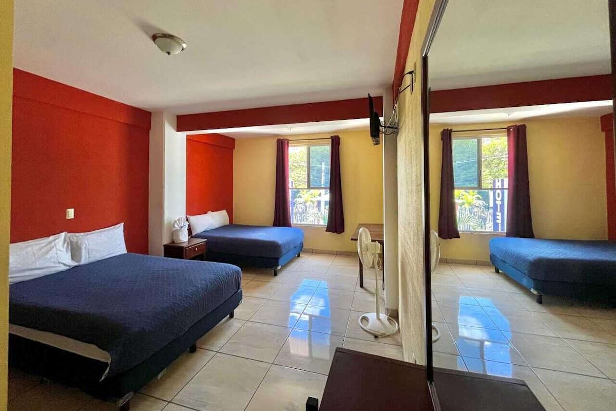 Ein Hotelzimmer mit zwei Betten, einem kleinen Tisch, einem Ventilator und einem Fenster mit Vorhängen.