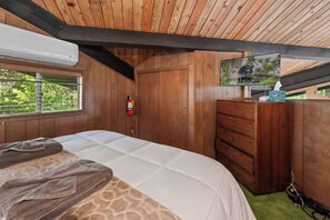 A wooden cabin room with a bed, a dresser, a television, and a window with blinds.