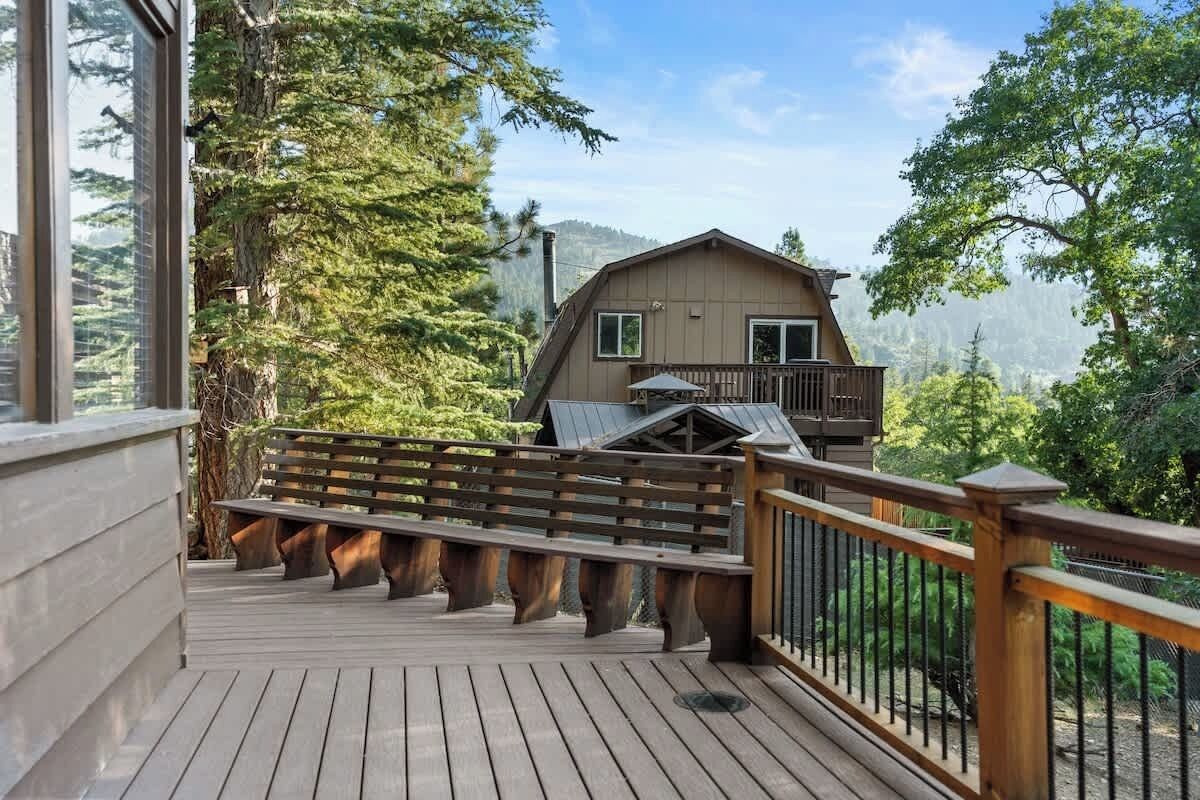 Une terrasse en bois avec une rambarde, une maison dotée d’un balcon et un paysage boisé en arrière-plan.