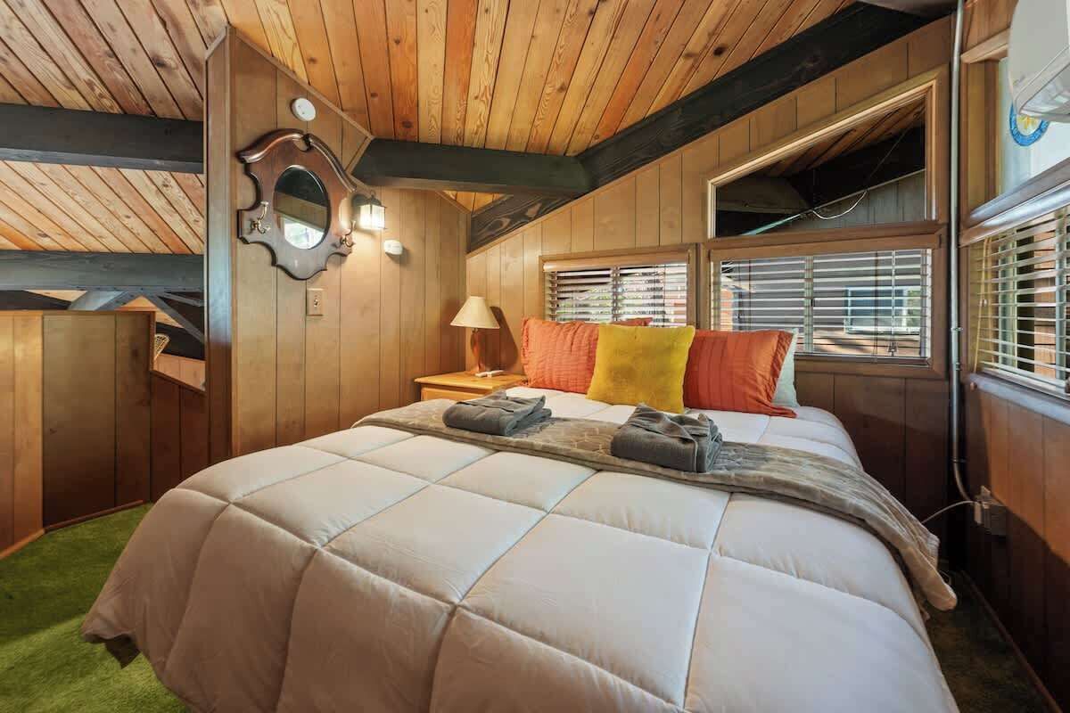 Un dormitorio acogedor con una cama grande, paredes de madera, un espejo y una ventana con persianas.