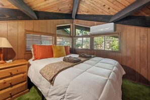 Een slaapkamer met houten lambrisering, een bed, kussens, een lamp en een raam.