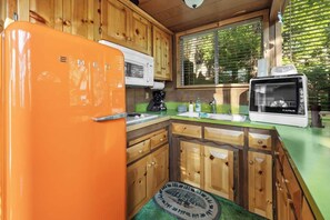 A compact kitchen with wooden cabinets, a green countertop, a white microwave, and a small refrigerator. - Retro Bear Haus • Spa • Fully Fenced (Big Bear Lake)