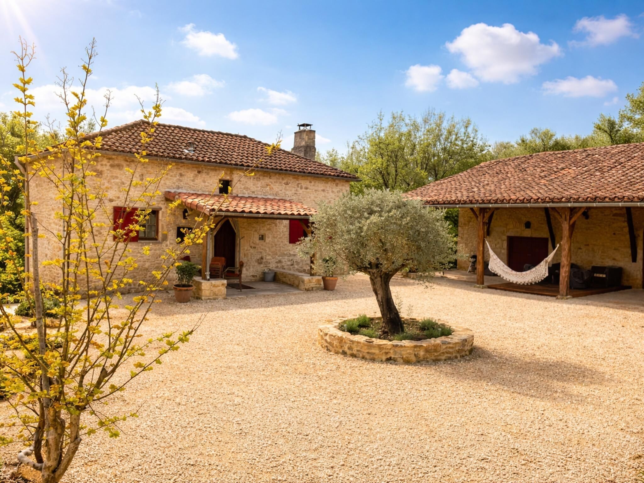 A stone building with a tiled roof, a hammock, and a small tree in the center.