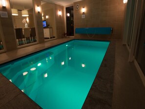 A swimming pool with a blue tint, surrounded by a tiled wall and a reception area with a television.