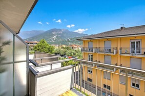 Ein Balkon mit Blick auf ein gelbes Gebäude, einen Berg und weitere Wohnhäuser.