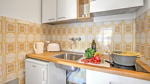 A kitchen with a sink, a toaster, a small refrigerator, and a stove with a pot of spaghetti.