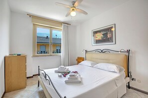 A neatly made bed with white linens, a ceiling fan, a window with curtains, a wooden wardrobe, and a framed picture on the wall. - Casa Silvia 50m From The Lake (Arco)