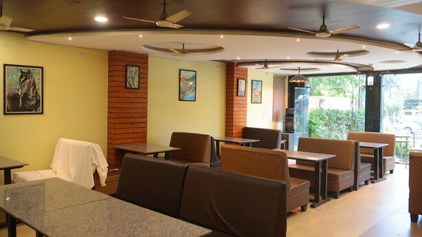 A restaurant with booths and tables, ceiling fans, and framed artwork on the walls. - Green Valley Palace (Bhopal)