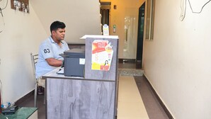 A man sitting at a desk with a computer and a poster advertising a promotion. - Green Valley Palace (Bhopal)