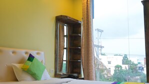 A hotel room with a bed, a window with curtains, a wooden headboard, and a view of buildings and power lines outside. - Green Valley Palace (Bhopal)