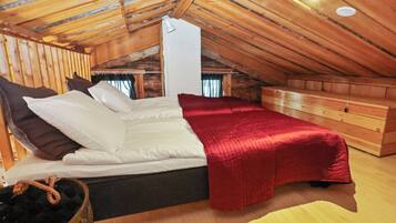 Un dormitorio con techo inclinado, paredes de madera, una cama con ropa de cama blanca, una manta roja y un aparador de madera.
