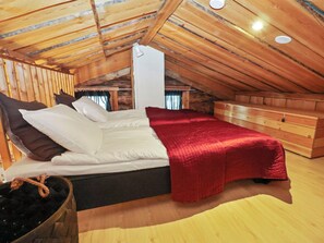 A bedroom with a sloped ceiling, wooden walls, a bed with white bedding, a red blanket, and a wooden dresser. - Kelorakka 9 by Interhome (Kittilä)