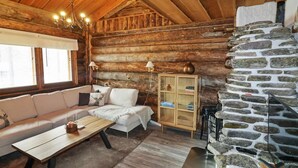 Tunnelmallinen hirsihuvilan sisustus, jossa on kivitakka, puuseinät, sohva ja ruokapöytä.