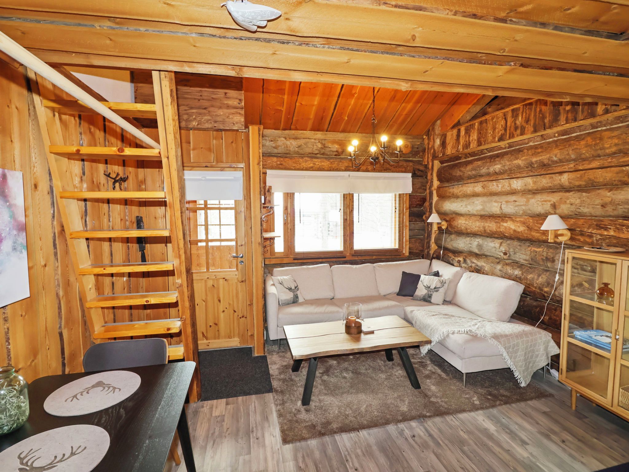 Interior acogedor de una cabaña, con paredes de madera, un sofá, una mesa, una lámpara y una escalera.