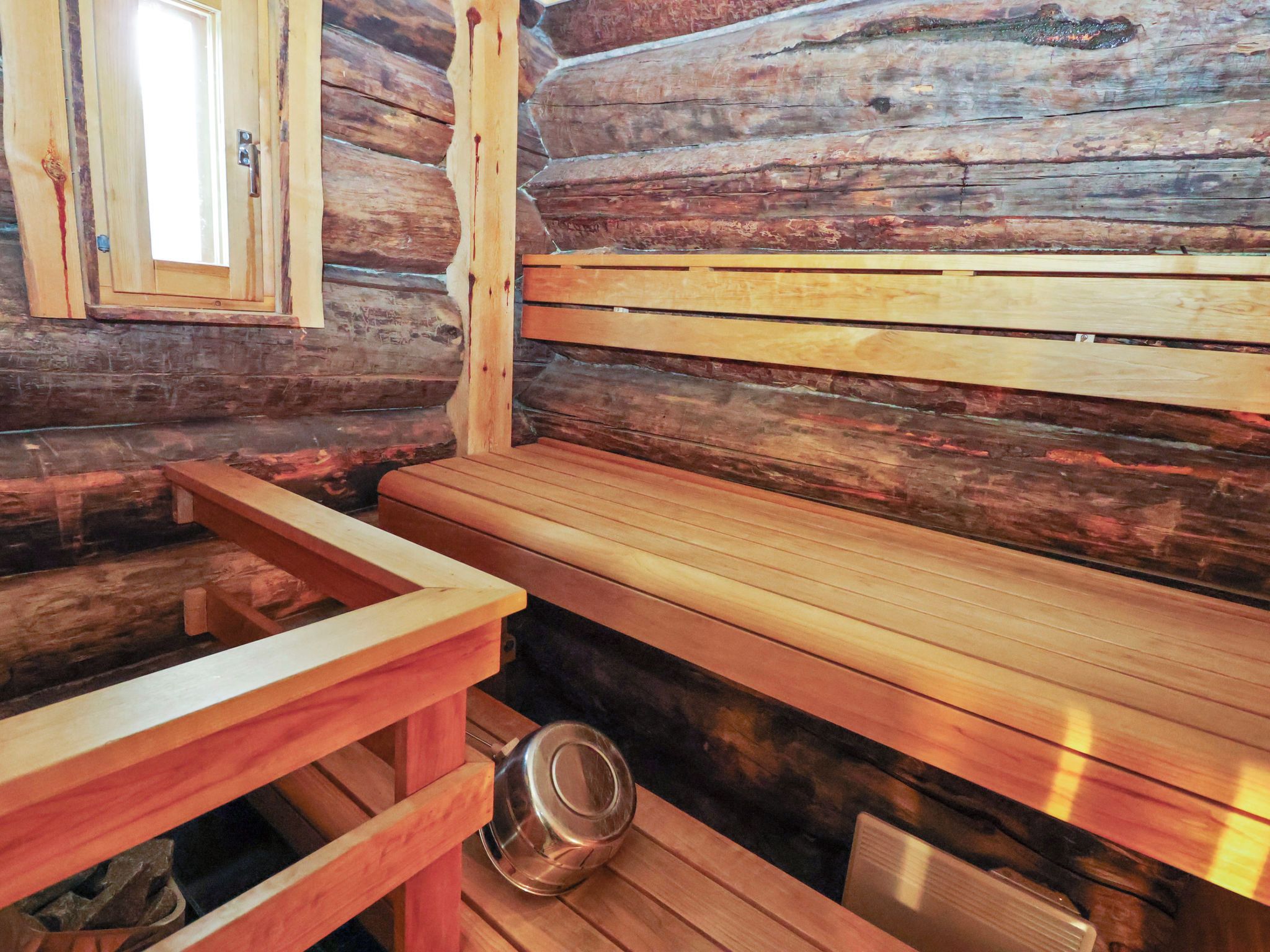 Puinen sauna, jossa on penkit ja metallinen säiliö, todennäköisesti vettä tai höyryä varten.
