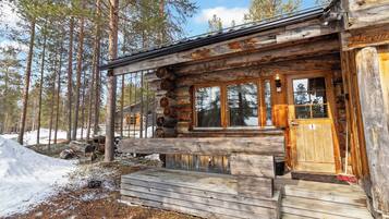 A log cabin with a wooden porch, large windows, and a door with a number plaque.