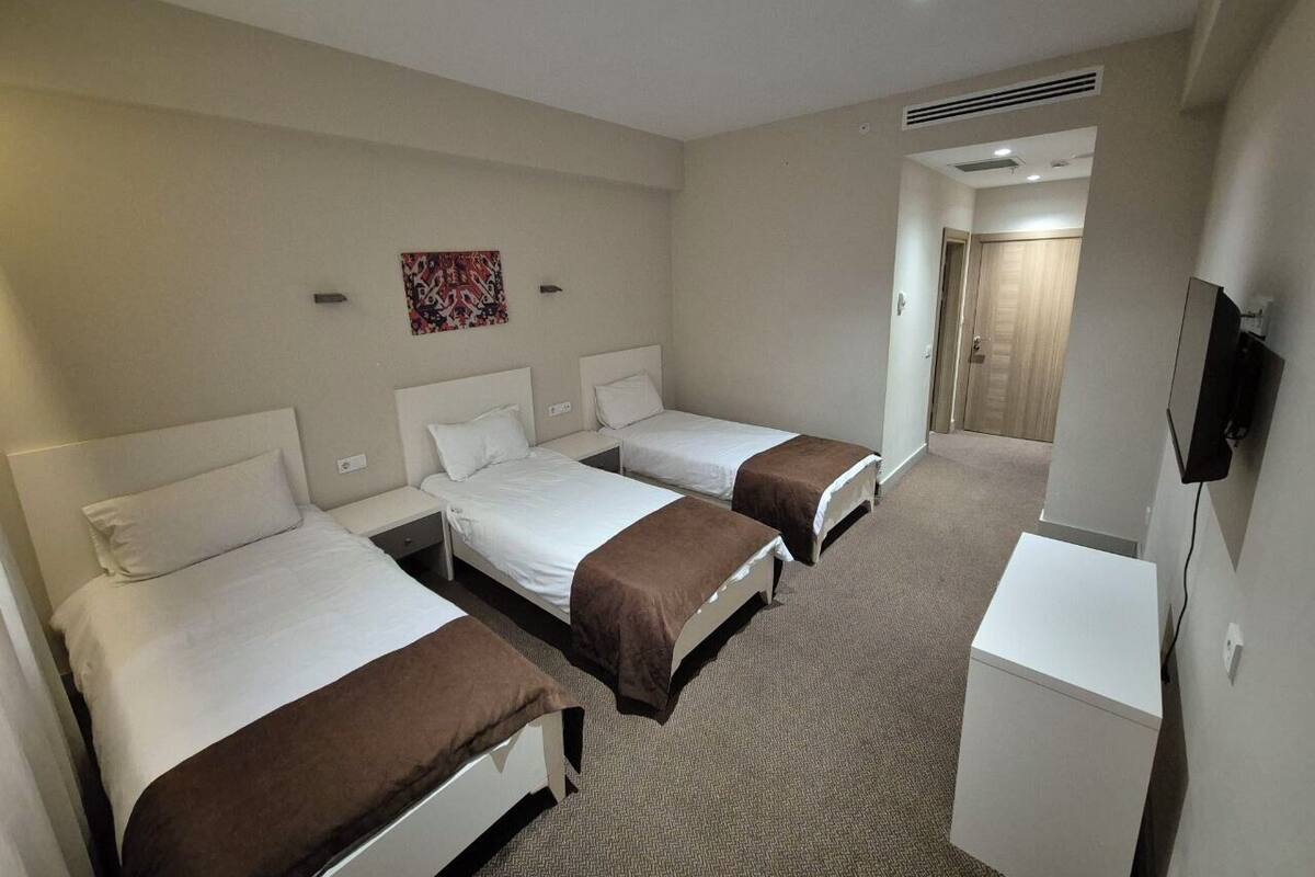 Une chambre d’hôtel avec trois lits simples, un petit bureau et un téléviseur.