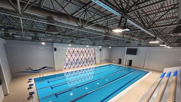 Piscina interior con carriles de natación, bloques de salida y techo con vigas estructurales visibles.